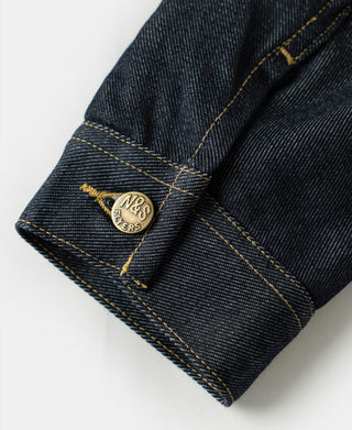 Indigo denim jacket cuff with yellow topstitching and circular brand patch