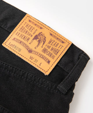 Orange leather patch label on black denim jeans with 'War It Ivory' text