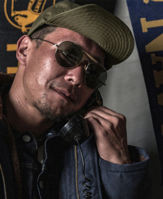Olive military cap with embroidered emblem, worn with aviator sunglasses