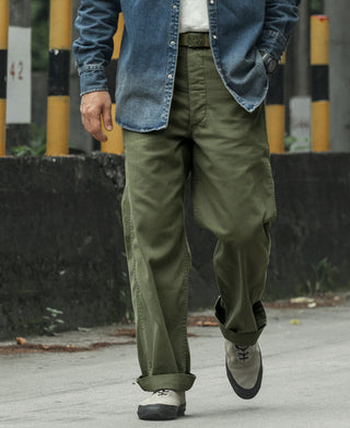 Olive fatigue trousers with relaxed fit and cuffed hems, side view on wearer