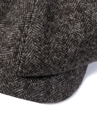 Dark gray wool newsboy cap brim with stitched edge and textured herringbone weave.