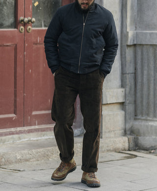  dark navy zip-up jacket, dark brown corduroy pants, and brown hiking boots, standing on a stone sidewalk in front of a red wooden door.