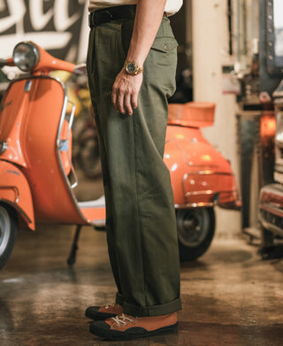 Olive cotton twill trousers worn with front pleats and cuffed bottom hem